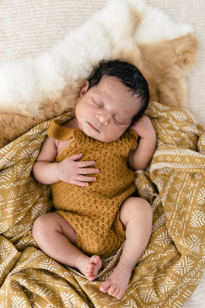 A newborn baby girl sleeps on a bed of fur and blankets 