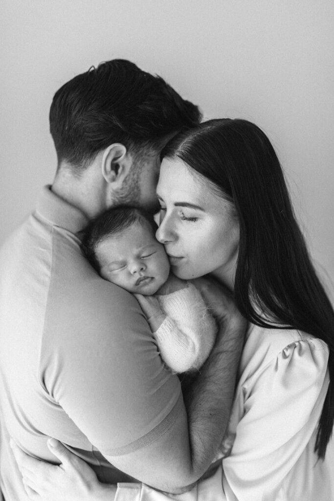 A couple hold thier newborn baby as mother kisses baby on the head 