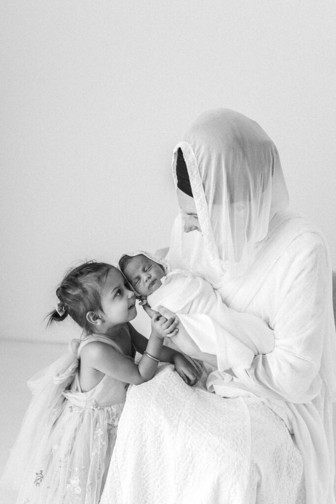 mother and daughter pose together with newborn baby, photograph in black and white 