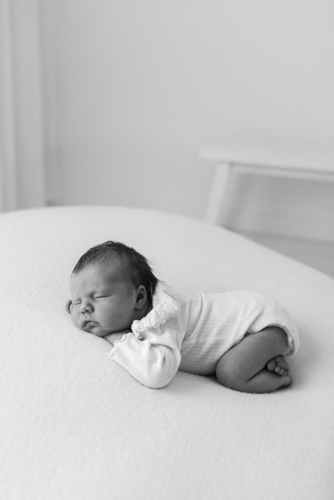 A newborn baby girl sleeps on here tummy, photograph in black and white 