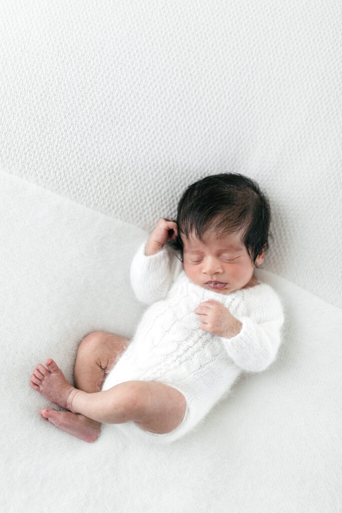 newborn baby wearing white sleeps on beanbag 