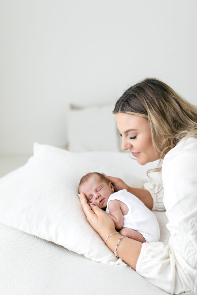 newborn baby lies ona  neanbag and the mother leans over them, cradling them in her arms as they sleep