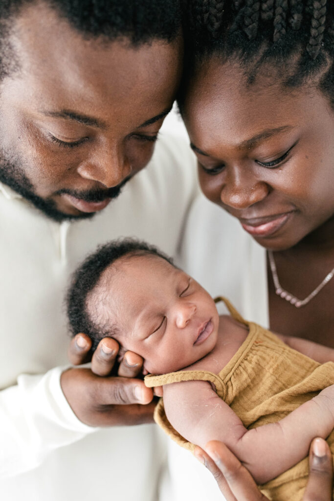 couple pose with thier neewborn baby who is asleep in thier arms 