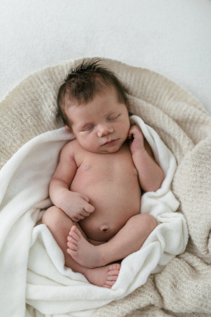 Newborn baby lies sleeping on a bed of blankets 