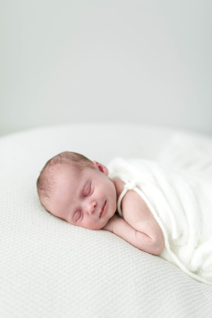 baby sleeping on thier front wrapped in a white blanket 