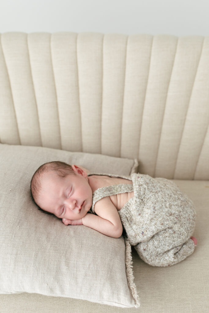 newborn baby sleeping on thier stomach ontop of a pillow wearing fluffy clothes