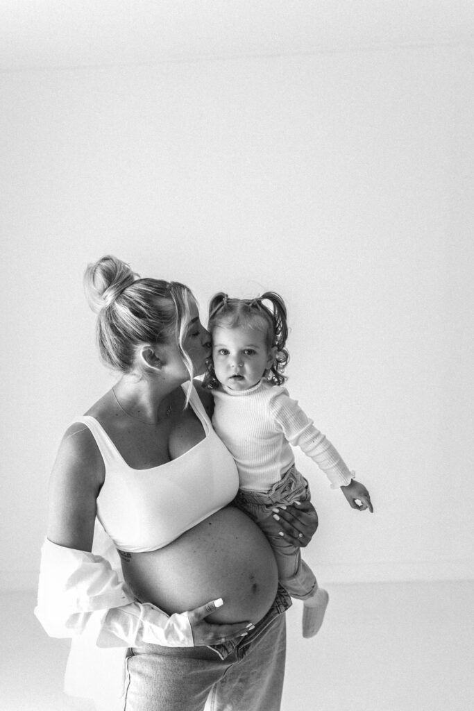 Black and white image of pregnant mother kissing her toddler onthe cheek 