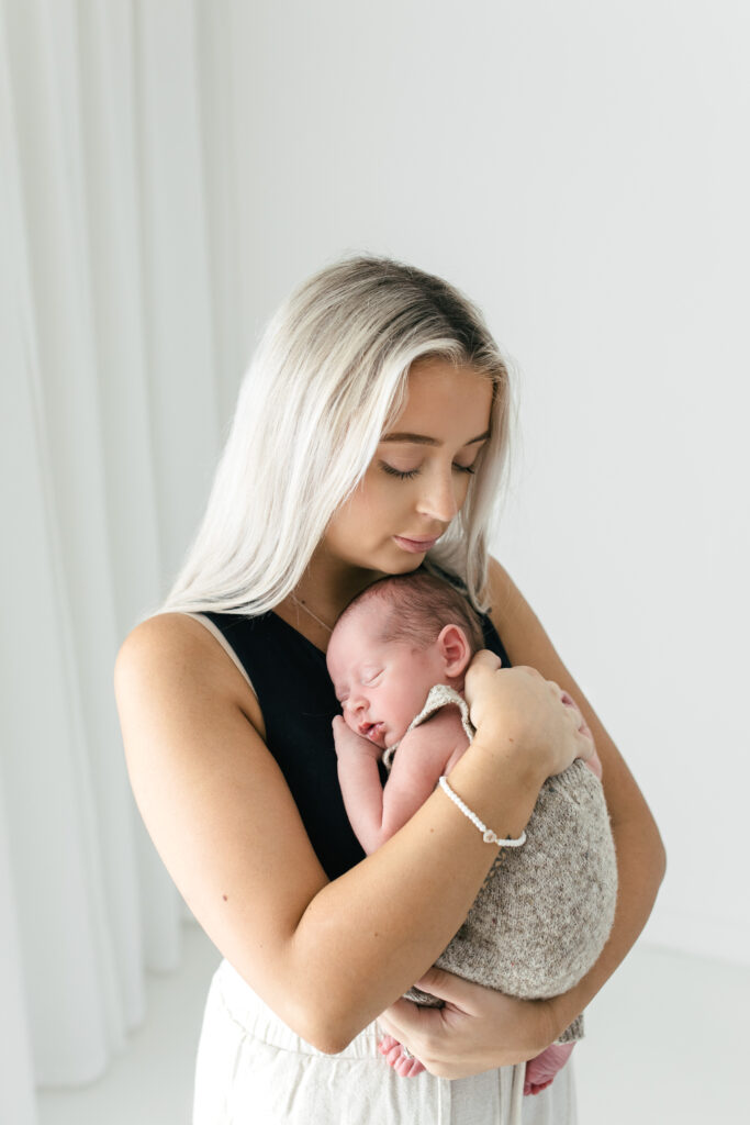 Mother and newborn baby cuddle together with thier eyes closed 