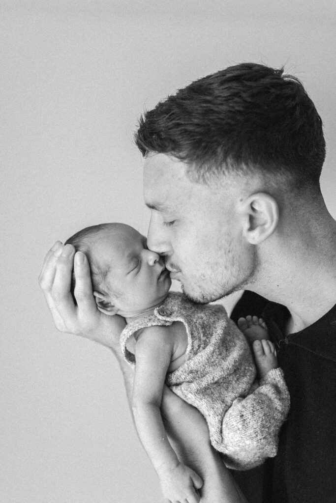 Dad holds newborn baby in his arms and is kissing him on the forehead 