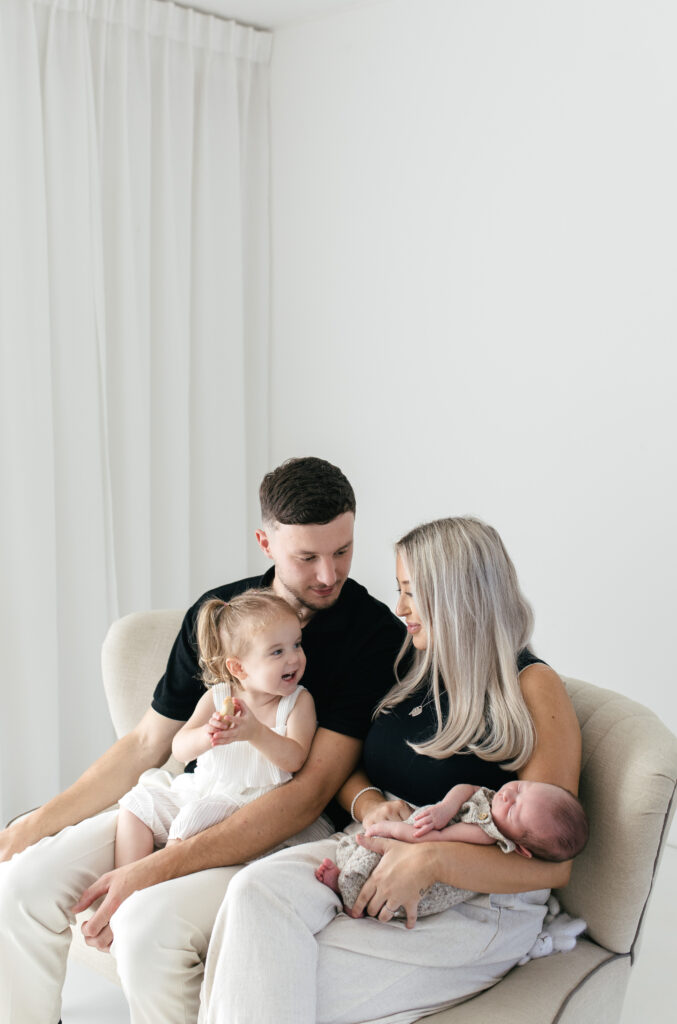 Famiyl of four sat on a sofa and cuddling together, the toddler is smiling at her mother 