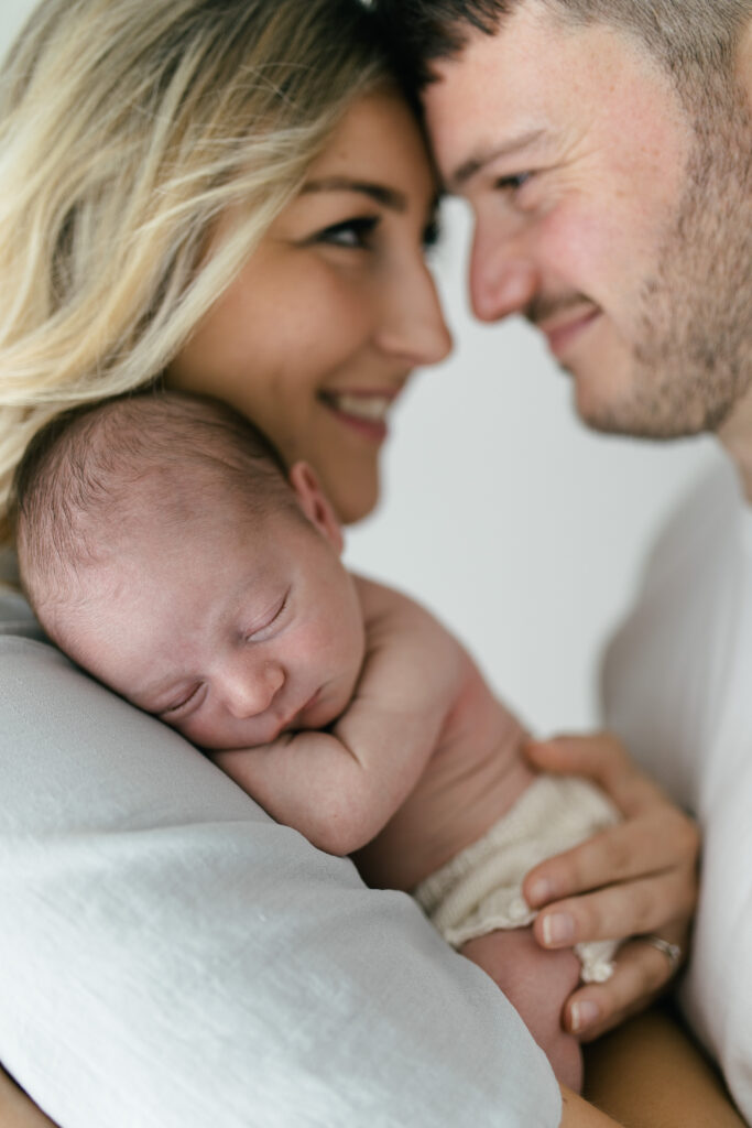 Mother and father cuddle newborn baby together during photoshoot