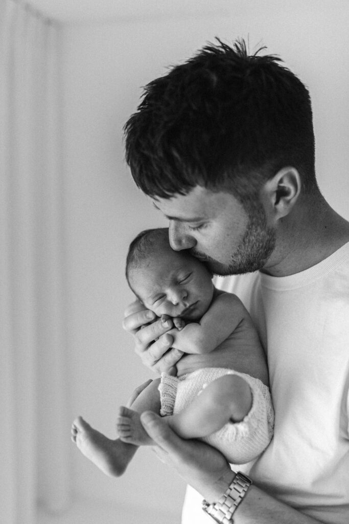 Dad kisses newborn baby on the head natural relaxed photograph