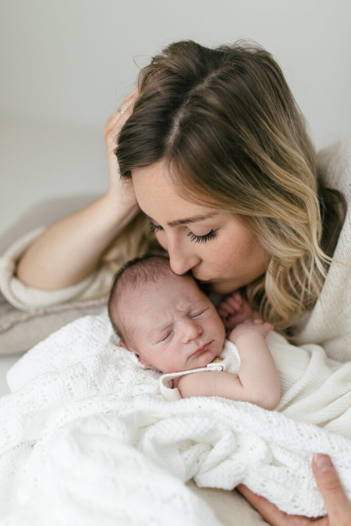 Newborn photoshoot mother kisses baby on the head 