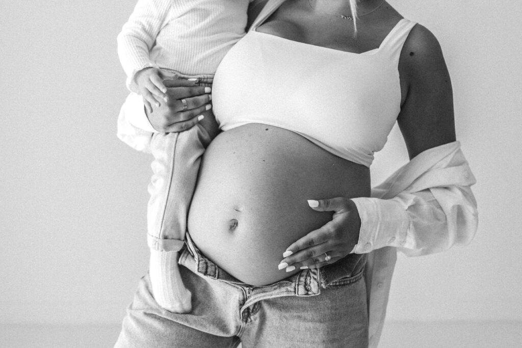 Pregnant woman holds her toddler in one hand and her pregnant belly in the other