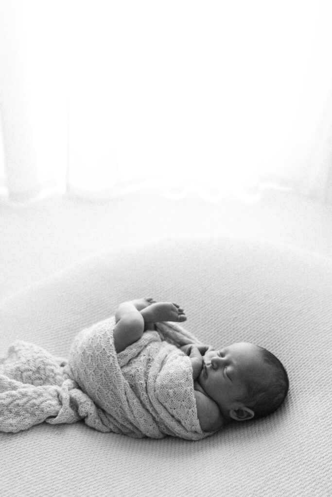 newborn baby sleeps on a beanbag in an all white photography studio, image is very natural and relaxed, edited in black and white 