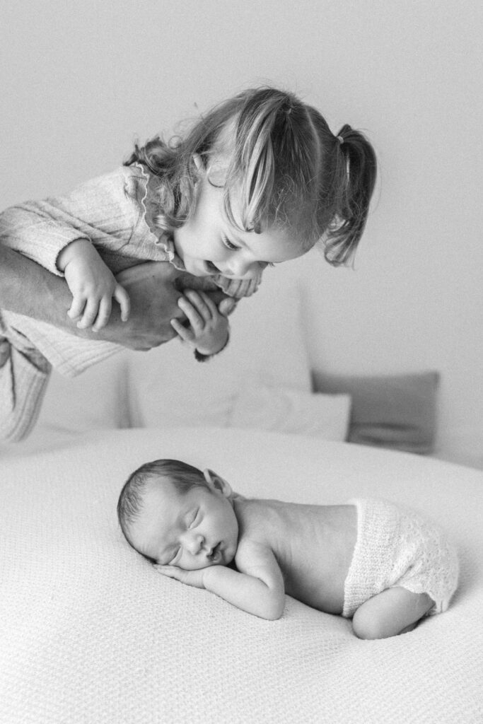 newborn baby boy sleeps on his belly whilst his toddler sister is held over him 