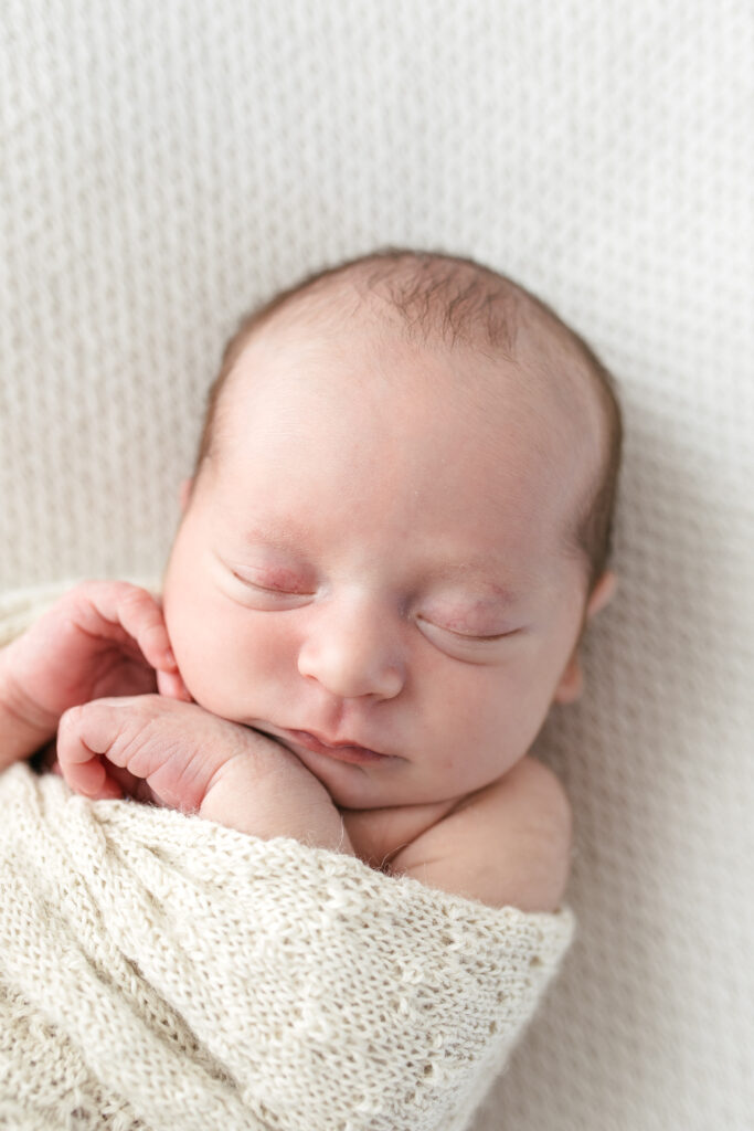 Newborn baby boy is sleeping and swaddled in a cream blanket 