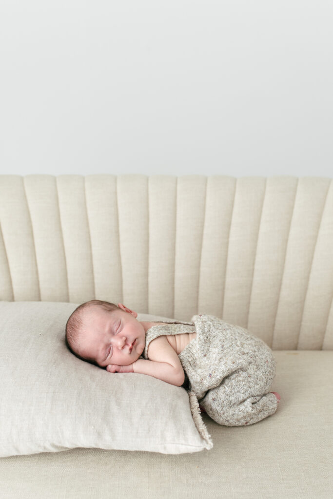 Newborn boy is lying on a cushion, on his belly ontop of a cream sofa 