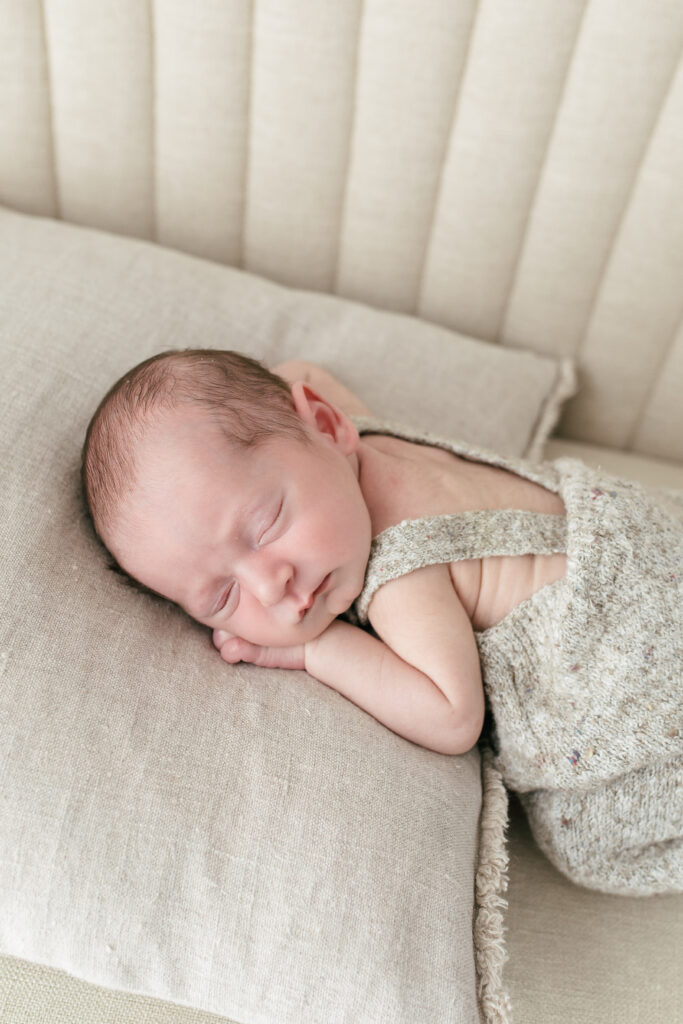 Newborn baby boy lies on his tummy ontop of a cushion 